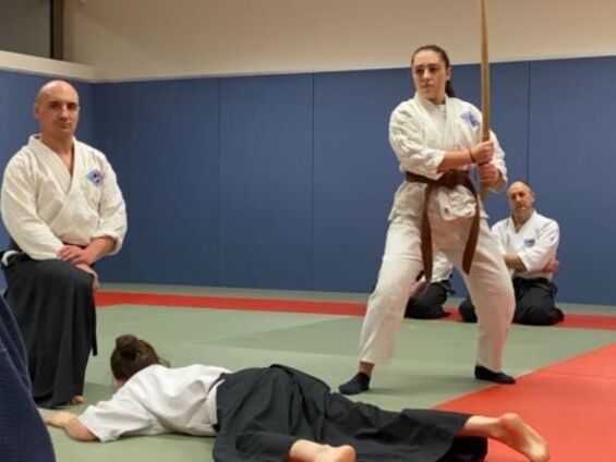 Sarah Durez tenant un sabre en bois, avec une condisciple allongée sous le regard de deux instructeurs
