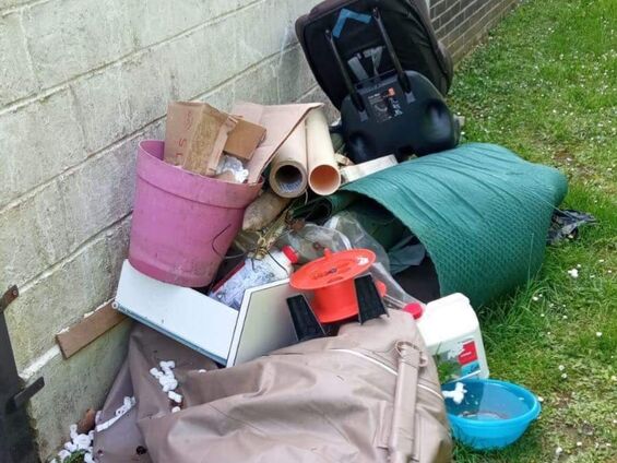 Divers déchets posés sur l'herbe, contre un mur
